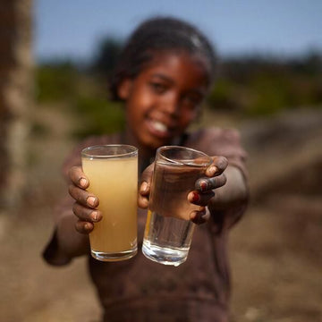 Child holding two glasses of water, one clear and one brown, outdoors.